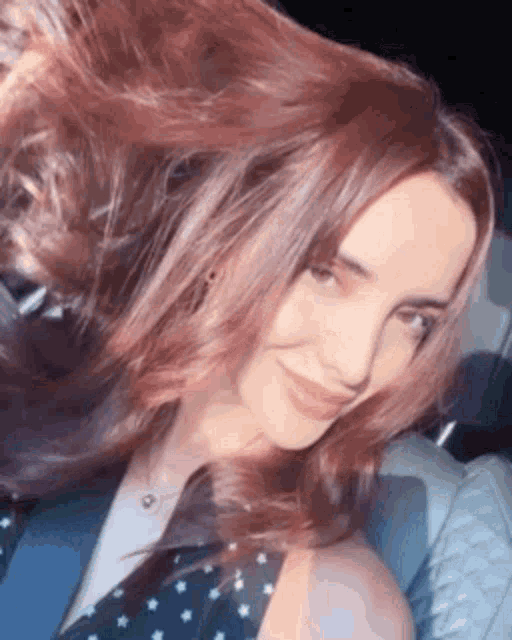 a woman with long red hair is smiling while sitting in a car .