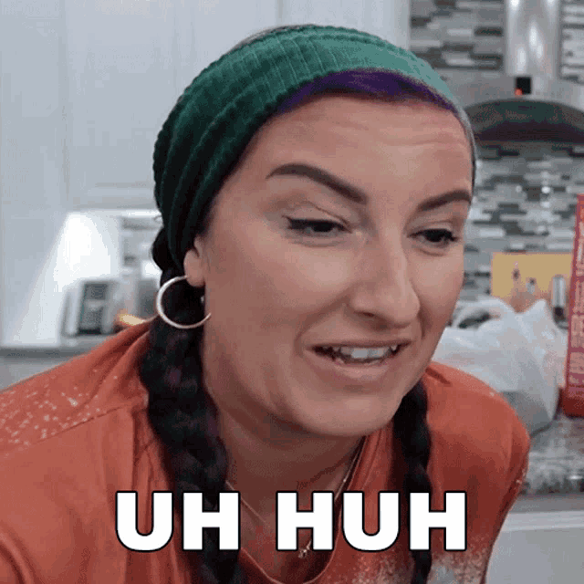 a woman with purple hair wearing a green headband and earrings says uh huh