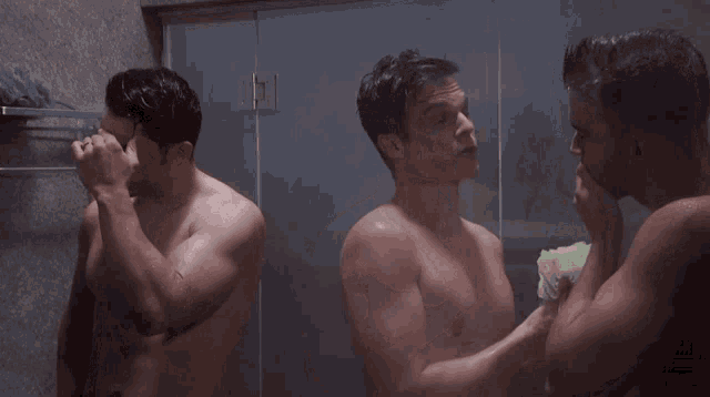 three shirtless men are taking a shower together and one is using a sponge