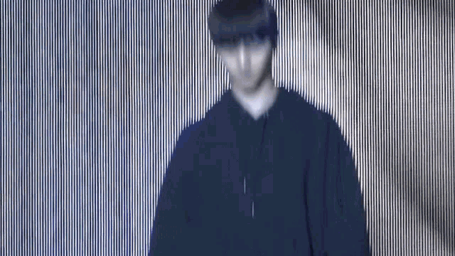 a blurry picture of a man in a black hoodie standing in front of a striped wall .