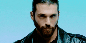 a man with a beard is wearing a leather jacket and looking at the camera .
