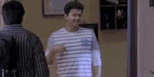 two men are standing next to each other in a room . one of the men is wearing a striped shirt .