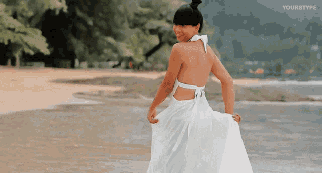a woman in a white dress is walking on a beach and the words yourstype are visible