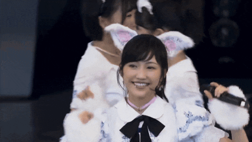 a girl wearing a cat ear headband is smiling while holding a microphone