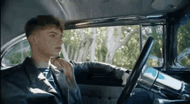 a young man is sitting in the driver 's seat of a car and looking out the window .