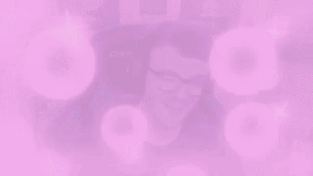 a man wearing headphones and glasses is sitting in a gaming chair with pink bubbles coming out of his head .