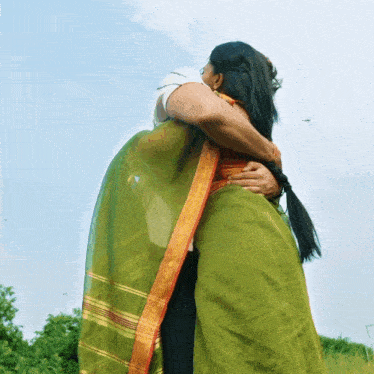 a woman in a green saree is hugging another woman in a white shirt