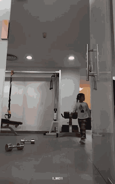 a little girl walking through a gym with x_mn211 written on the bottom right