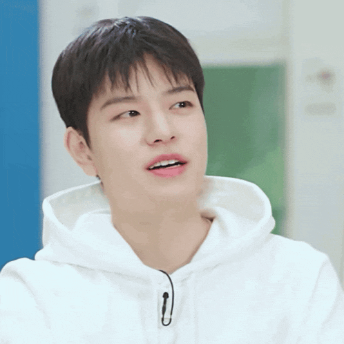 a young man wearing a white hoodie has a microphone attached to his ear