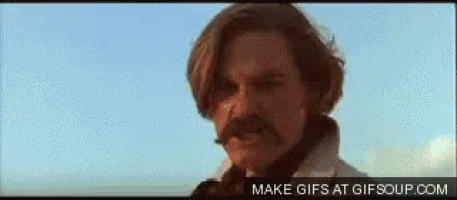a man with a mustache and long hair is looking at the camera .