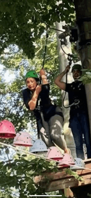 a woman in a green helmet is riding a ropes course in the woods .