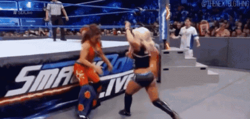 two women are wrestling in a wrestling ring with a referee in the background .