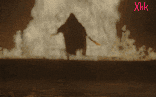 a silhouette of a person standing in front of a fire with xhk written on the bottom left