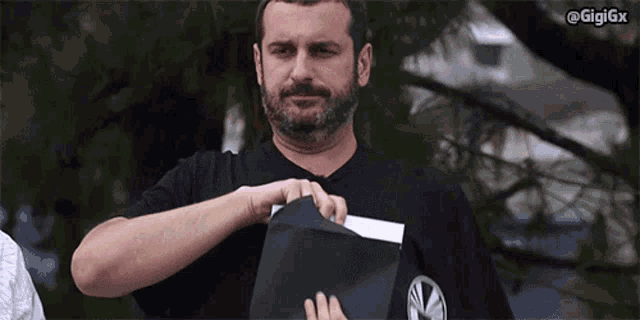 a man with a beard is holding a piece of paper with the hashtag gigigx at the top