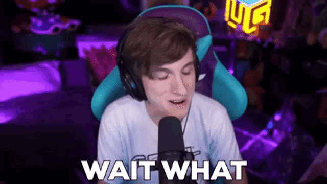 a man wearing headphones is sitting in front of a microphone with the words wait what written below him .