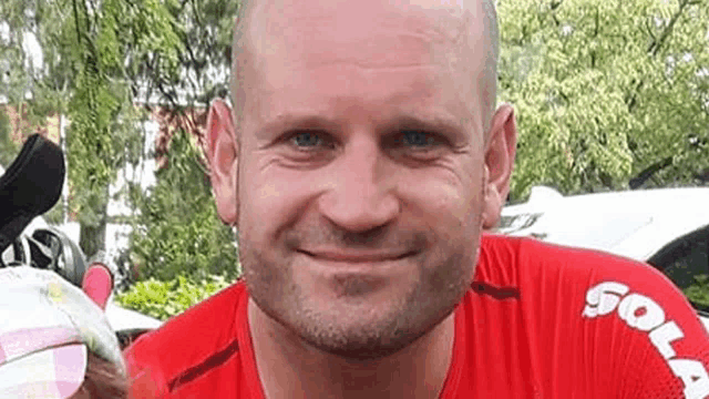 a bald man with a beard and a red shirt is smiling for the camera .
