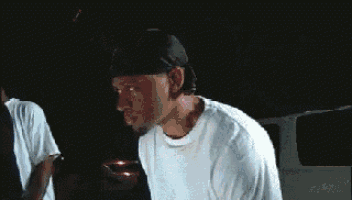 a man wearing a hat and a white shirt is standing in a dark room