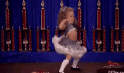 a little girl is dancing in front of trophies on a stage .