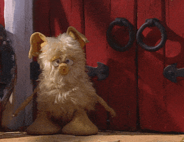 a stuffed animal standing in front of a red wooden door