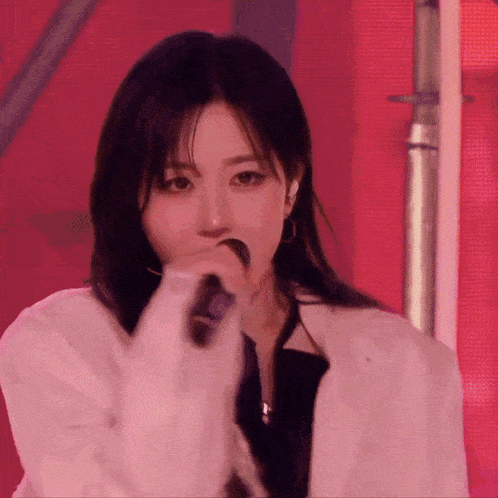 a woman is singing into a microphone while wearing a white jacket