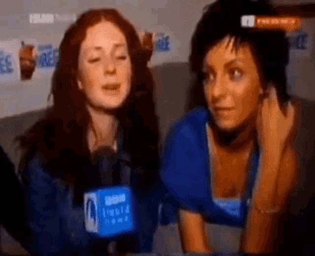 two women are sitting next to each other and talking into microphones .