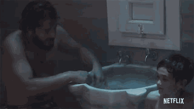 a young boy is taking a bath in a bathtub with a bucket of water .
