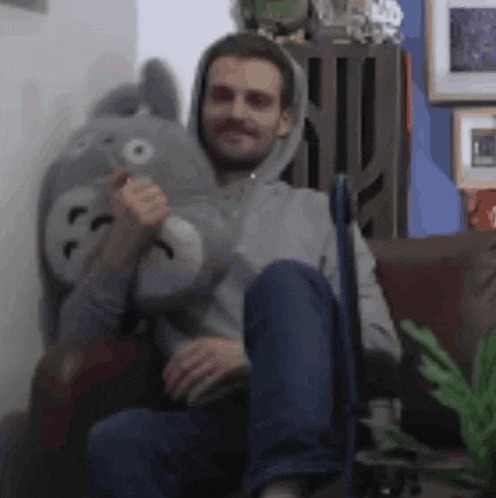 a man is sitting on a couch holding a stuffed animal that looks like a totoro