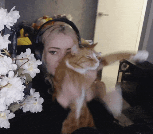 a woman wearing headphones holds an orange cat