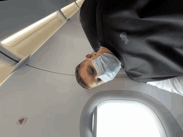 a man wearing a face mask and a north face vest on an airplane