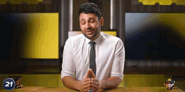 a man in a white shirt and tie is sitting at a table with a number 21 behind him