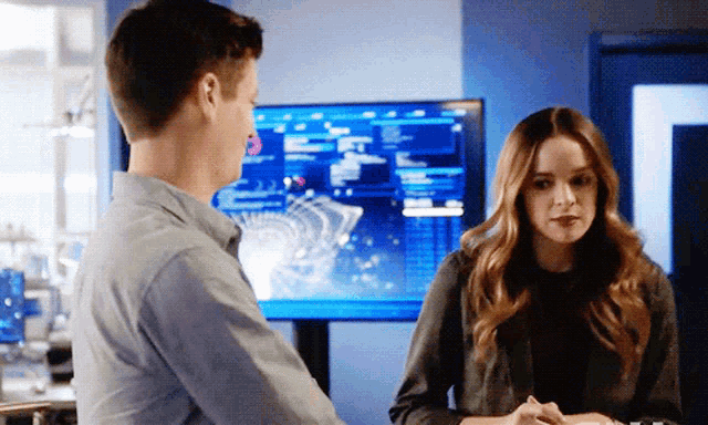 a man and a woman are standing next to each other in front of a large monitor .