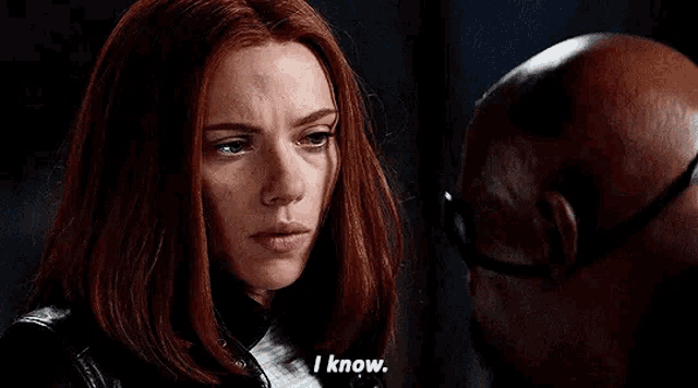 a woman with red hair is standing next to a bald man and talking to him .