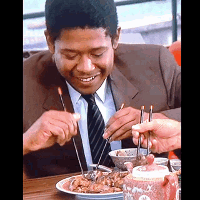a man in a suit and tie is eating a meal with chopsticks