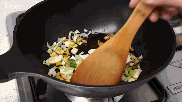 a person is stirring vegetables in a pan with a wooden spoon .