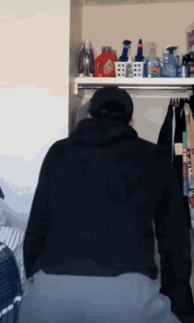 a man in a black hoodie is standing in a closet with clothes hanging on a rack