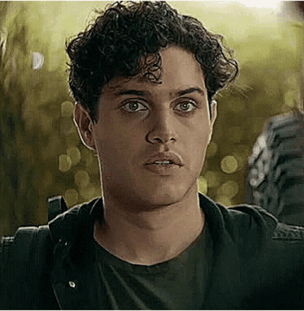 a young man with curly hair is wearing a black shirt and a black jacket and looking at the camera .