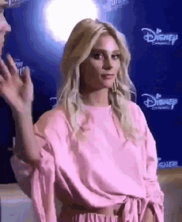 a woman in a pink top is standing in front of a disney sign .