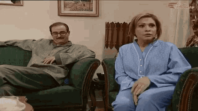 a man and a woman are sitting on a couch and looking at something .