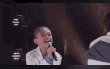 a young boy in a suit is singing into a microphone while talking to another person .