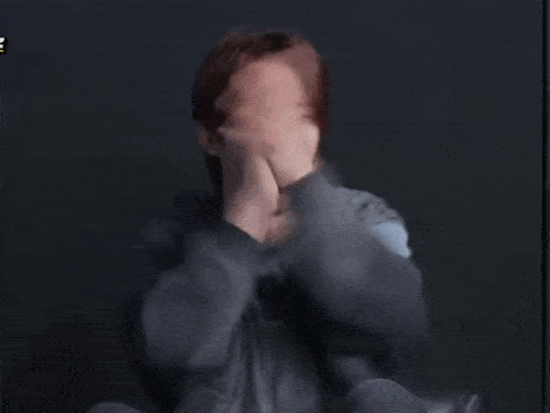 a man in a grey shirt is laughing with his hands in the air and a yellow sticker that says ' e '