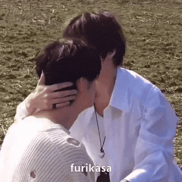 two men are kissing in a field and one of them is hugging the other .