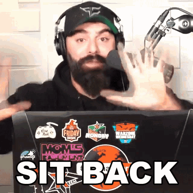 a man wearing headphones stands in front of a laptop that says sit back on it