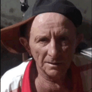 a close up of an older man wearing a hat and a red shirt .