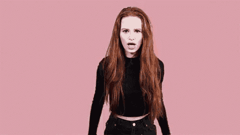 a woman with red hair is wearing a black crop top and black jeans and making a funny face .