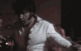 a man in a white suit is dancing on a stage in front of a microphone .