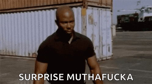 a man in a black shirt is standing in front of a shipping container and says surprise muthafucka .