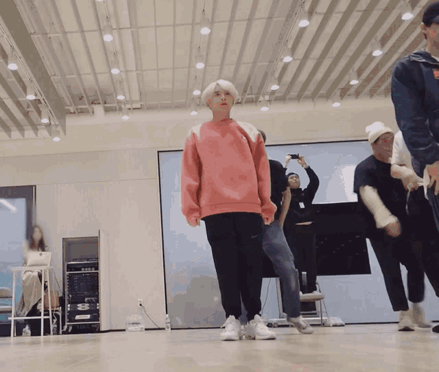 a woman in a pink sweatshirt is standing in a room with other people