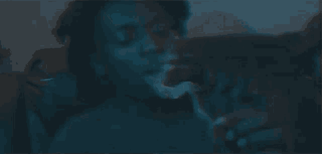 a man is smoking a cigarette in a dark room while sitting on a couch .