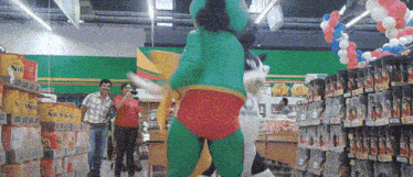 a mascot in a green and red outfit is dancing in a supermarket