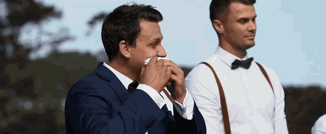 a man in a suit wipes a tear from his nose